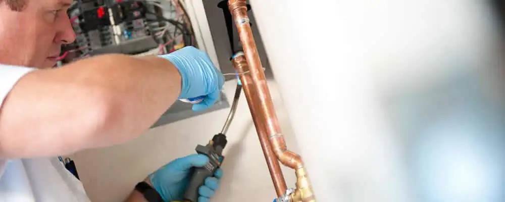 Water heater repair technician testing copper pipe connections and controls in Fresno, CA